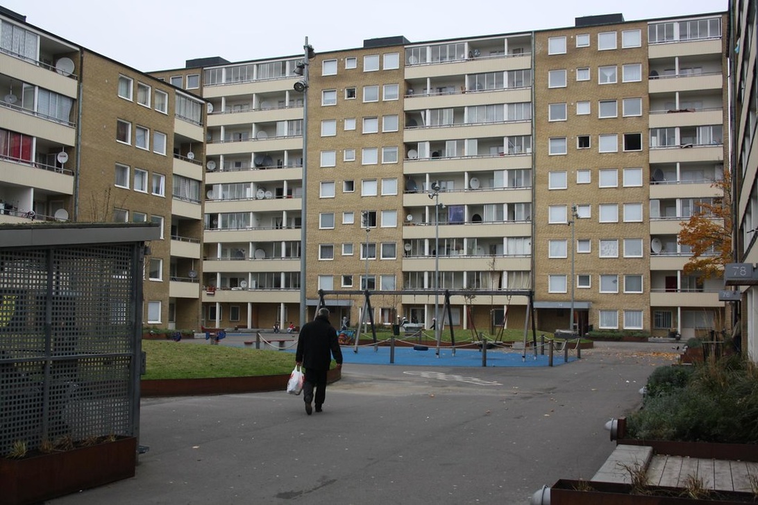 Ett stort lägenhetskomplex i Stockholm med beige tegelfasad, balkonger och en lekplats på innergården.